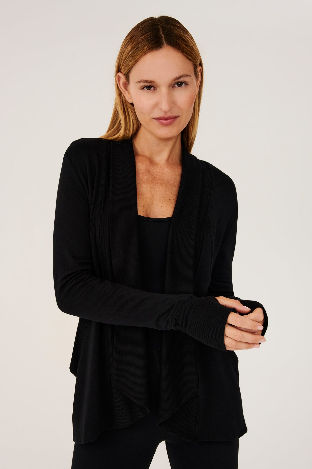 Front view of girl wearing black long sleeve open front flowy sweater with thumb holes on sleeve cuff and black top with black leggings