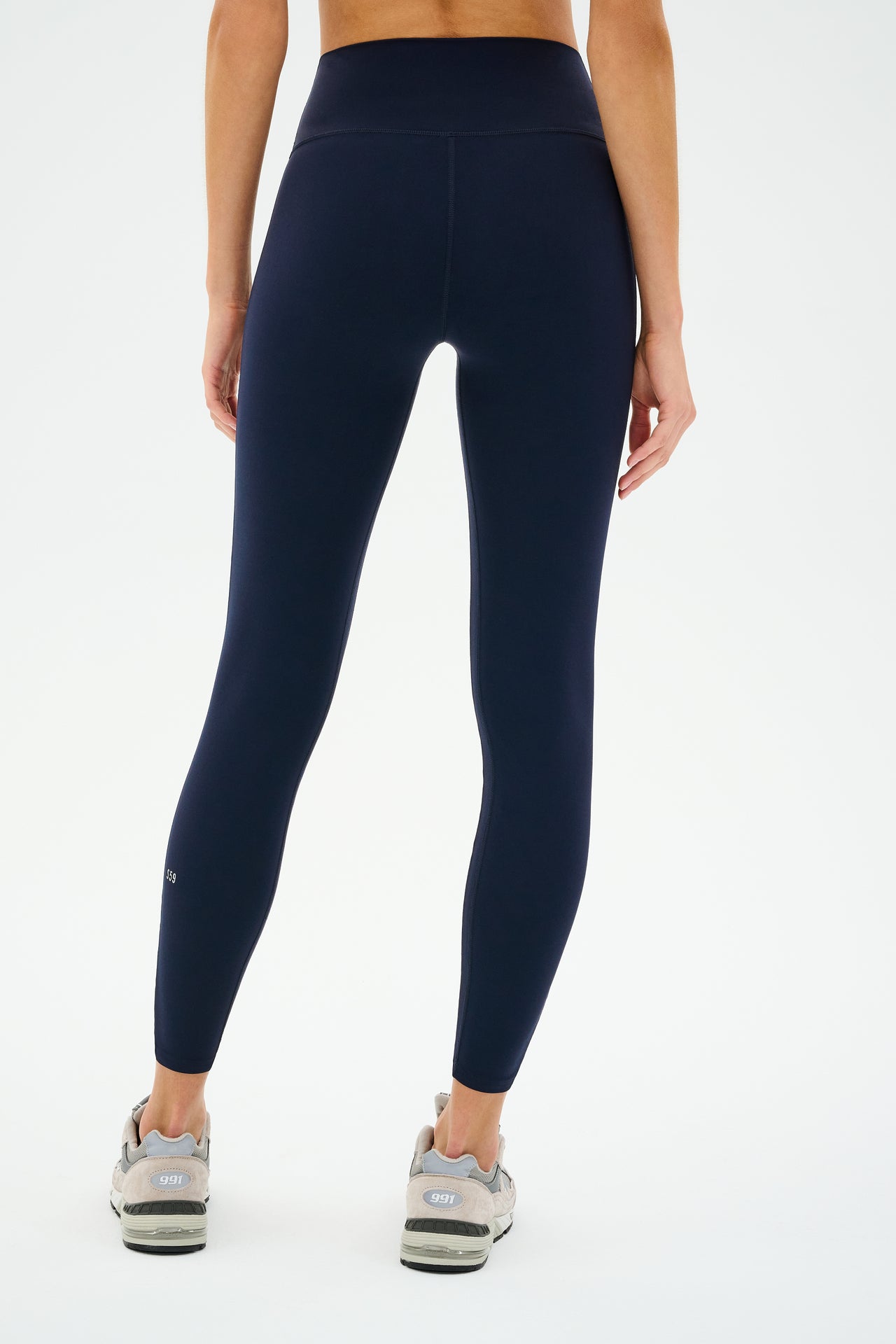 A person is shown from the back against a plain background, wearing SPLITS59 Chevron Airweight High Waist 7/8 leggings in Indigo/Latte and gray sneakers, highlighting the ultra luxe fabric.