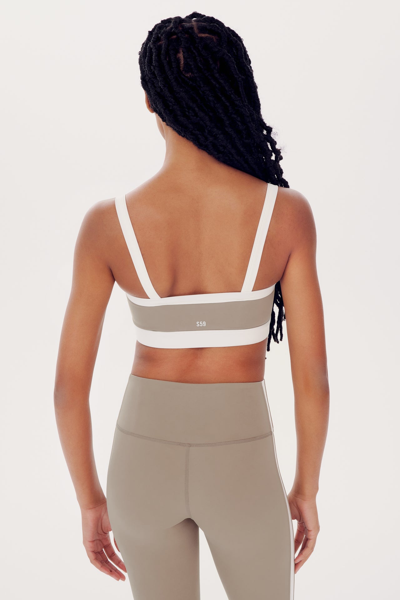 A woman from behind wearing a white SPLITS59 Monah Rigor Bra and beige leggings, highlighting athletic wear design.