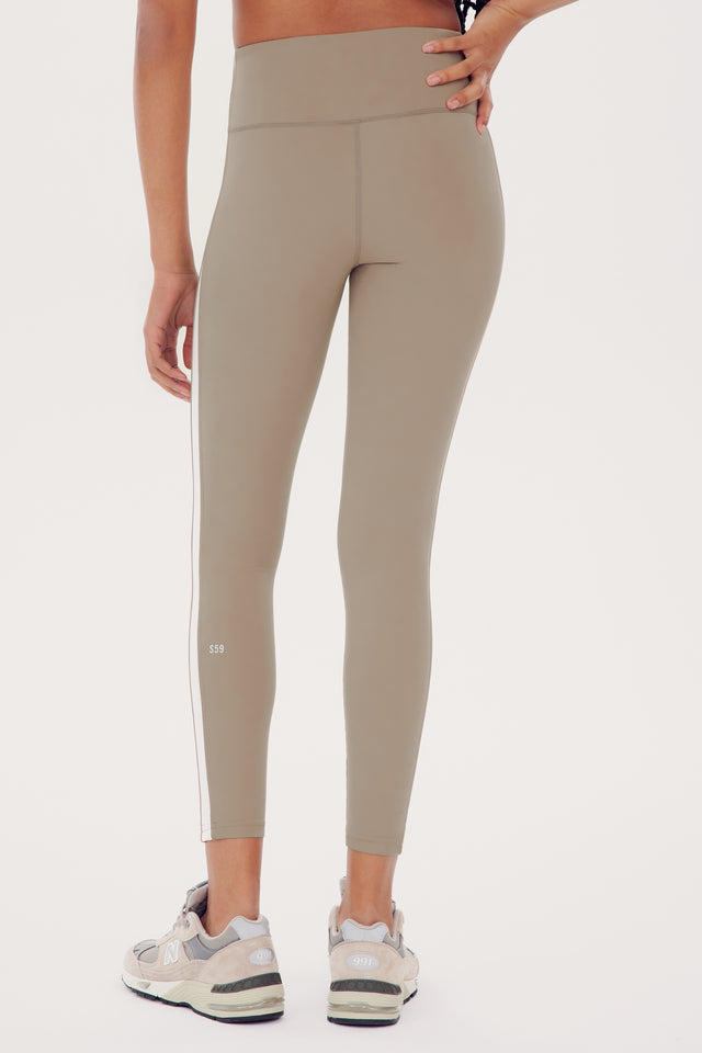 Woman wearing SPLITS59 Clare High Waist Rigor 7/8 leggings in Latte/White and white sneakers, viewed from the side, focusing on the lower half of her body.