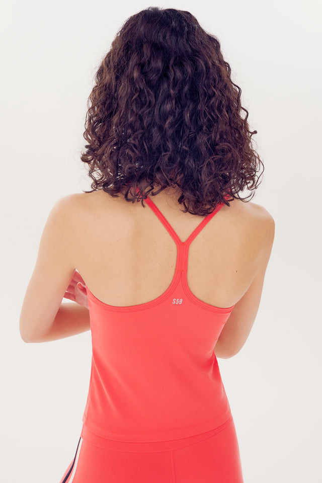 A woman with curly hair wearing a red nylon Airweight Tank in Melon by SPLITS59, viewed from behind.