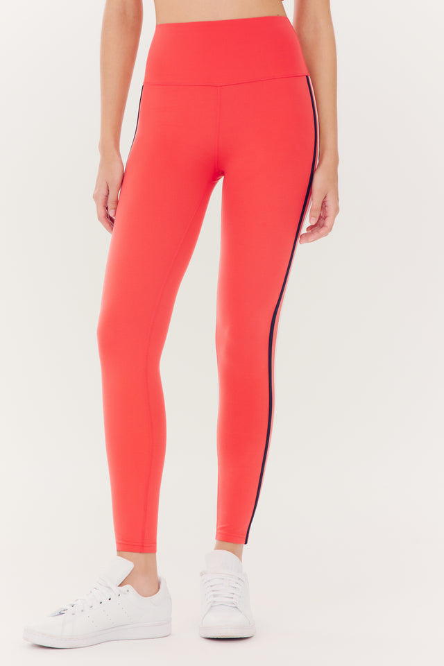 Person wearing red Ella High Waist Airweight 7/8 leggings with a side stripe and white SPLITS59 sneakers.
