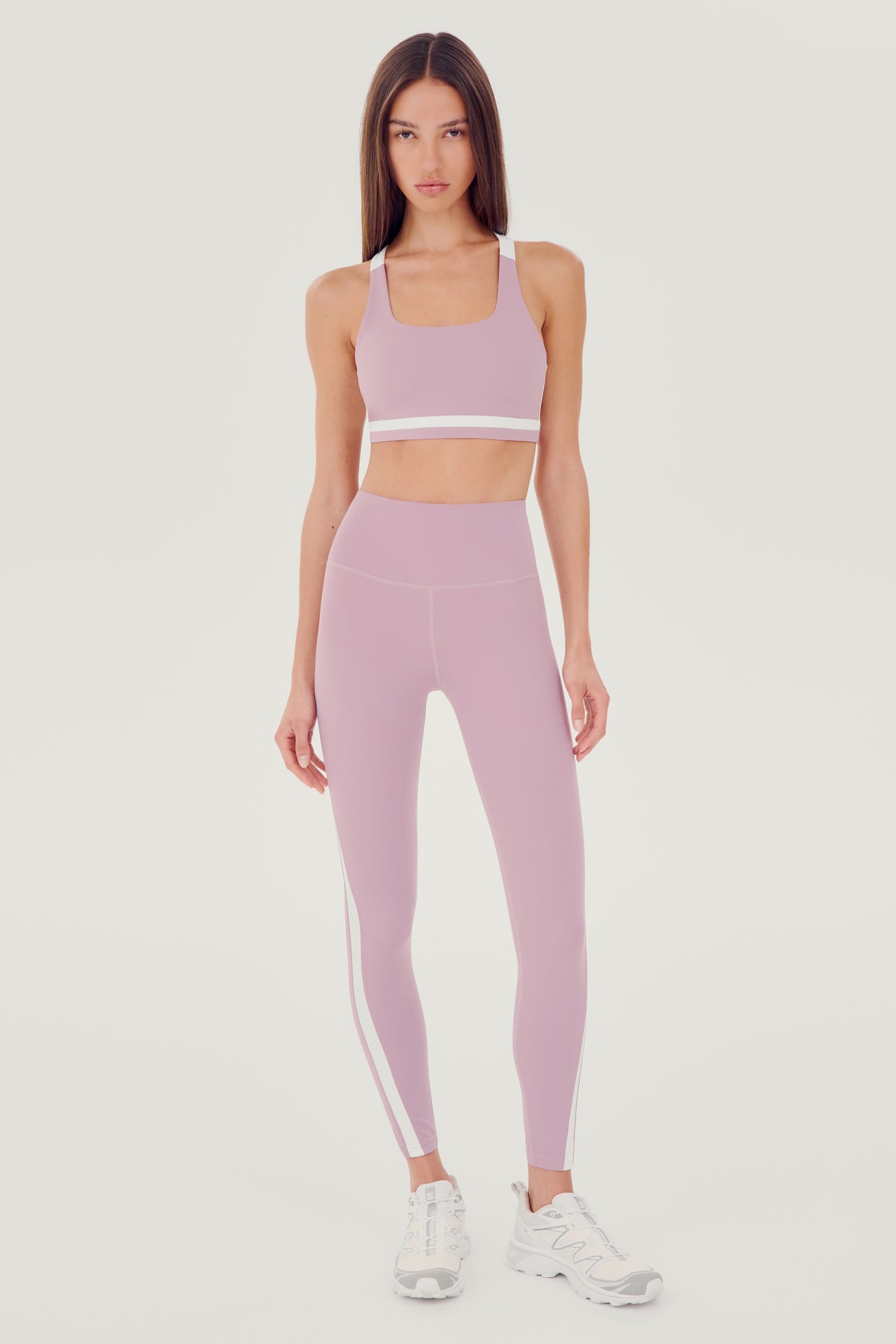 A woman wearing SPLITS59 Miles High Waist Rigor 7/8 - Blush/White sports bra and leggings, ready for her yoga session.