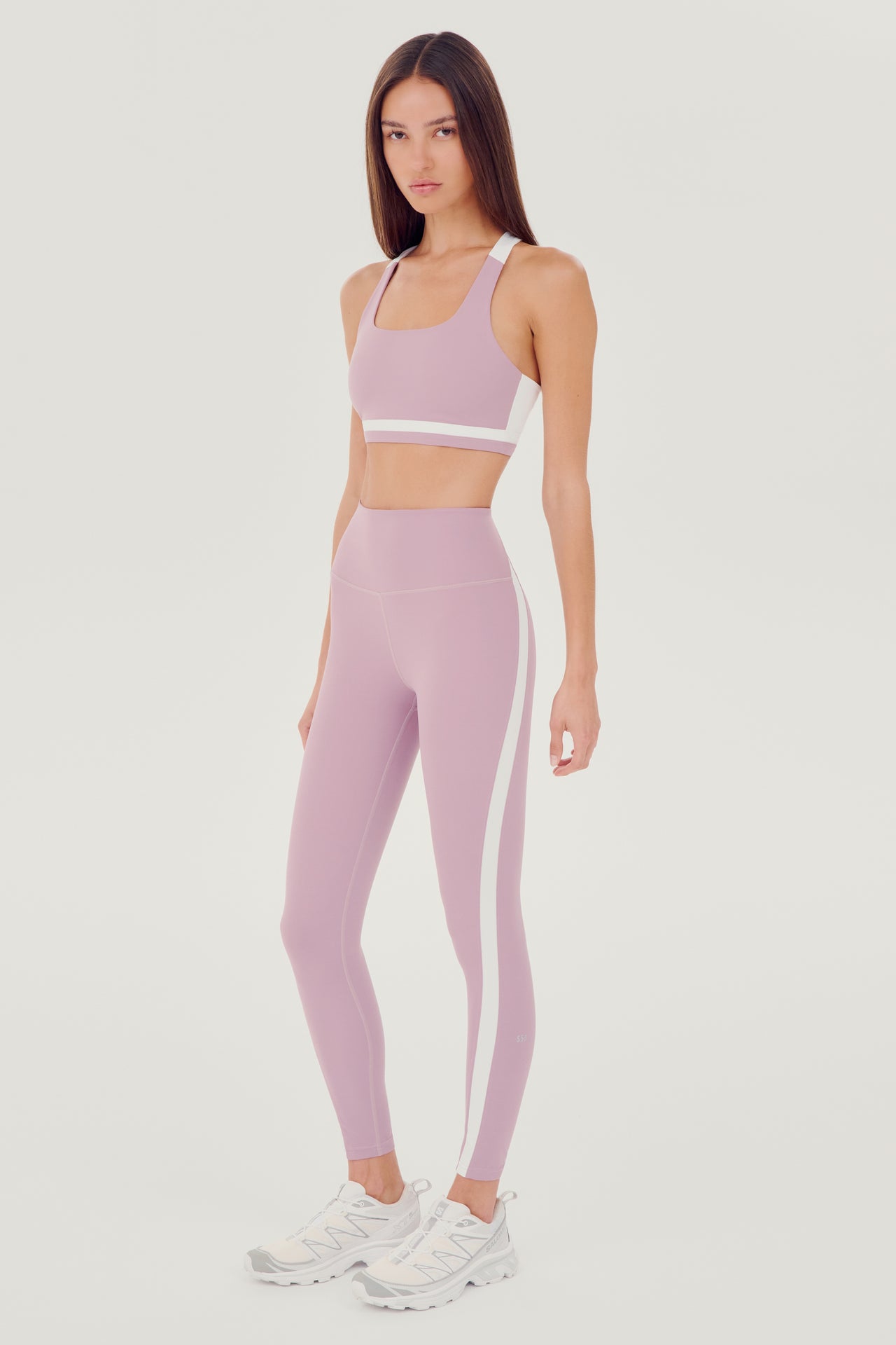 A woman wearing a SPLITS59 Miles Rigor Bra in Blush/White and leggings designed for style and support during workouts.