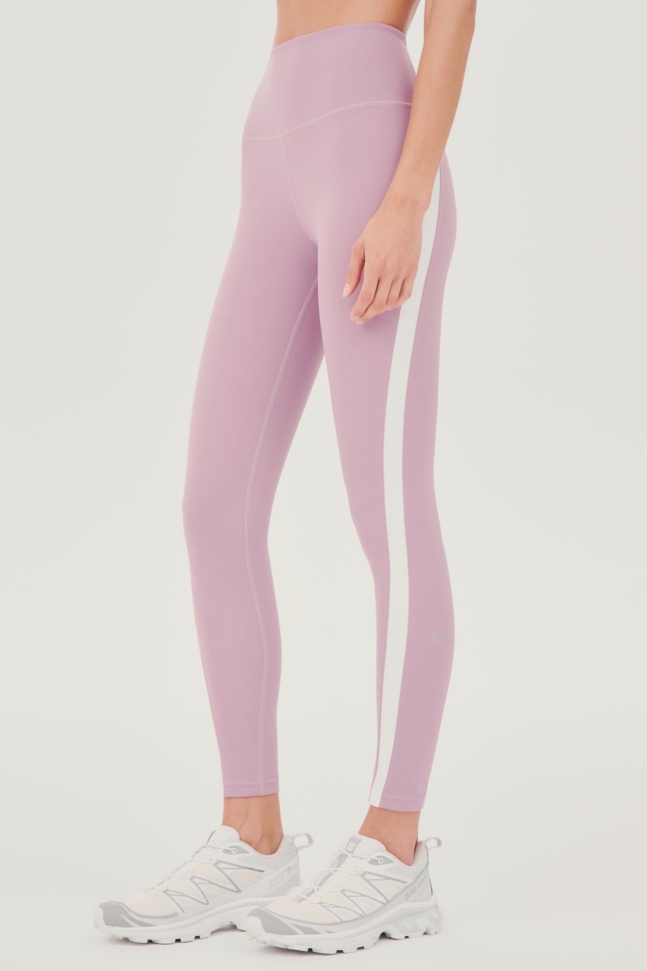 The back view of a woman wearing SPLITS59 Miles High Waist Rigor 7/8 - Blush/White leggings, ready for her yoga session.