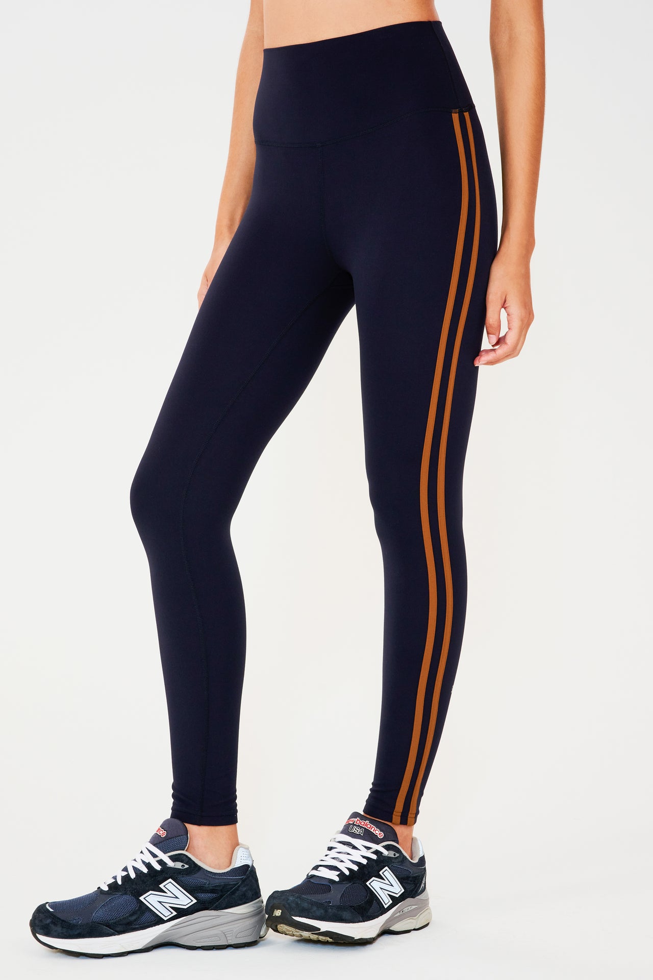 Front view of girl wearing dark blue leggings with two thin brown stripes down the side with dark blue shoes