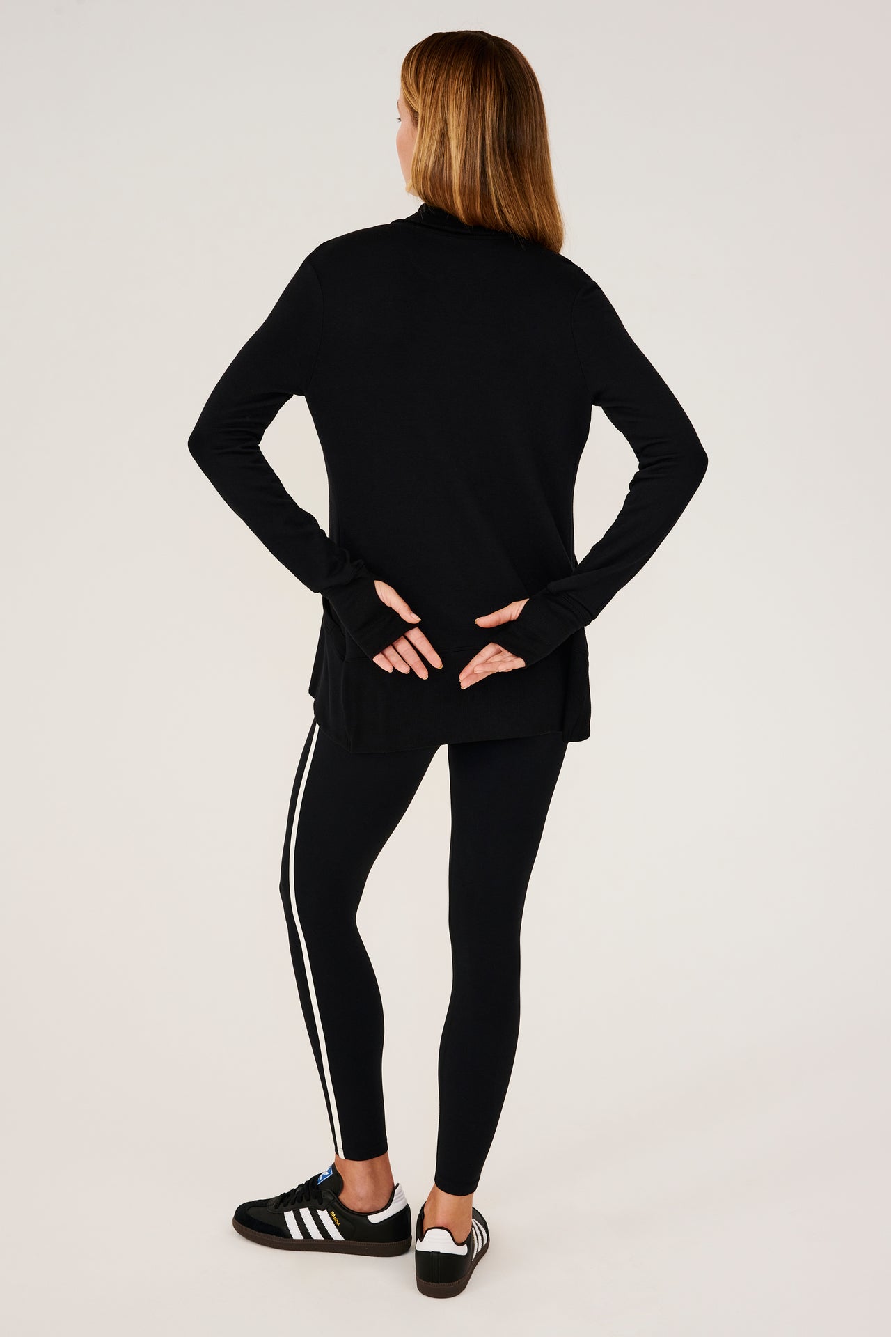 Full back view of girl wearing black long sleeve open front flowy sweater with thumb holes on sleeve cuff and black top with black leggings