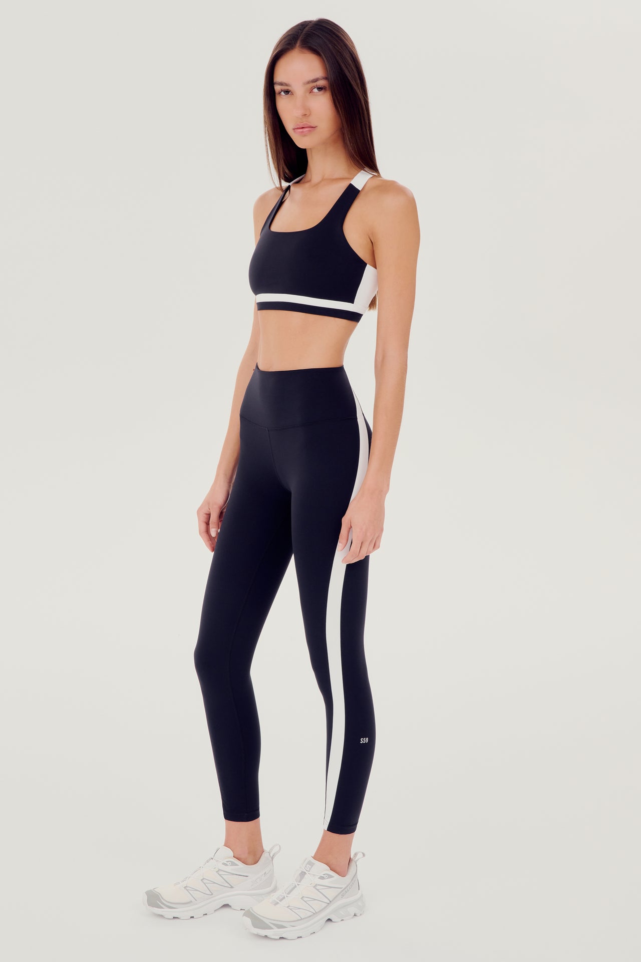 A woman wearing a SPLITS59 Miles Rigor Bra in Black/White with support and leggings, perfect for workouts.