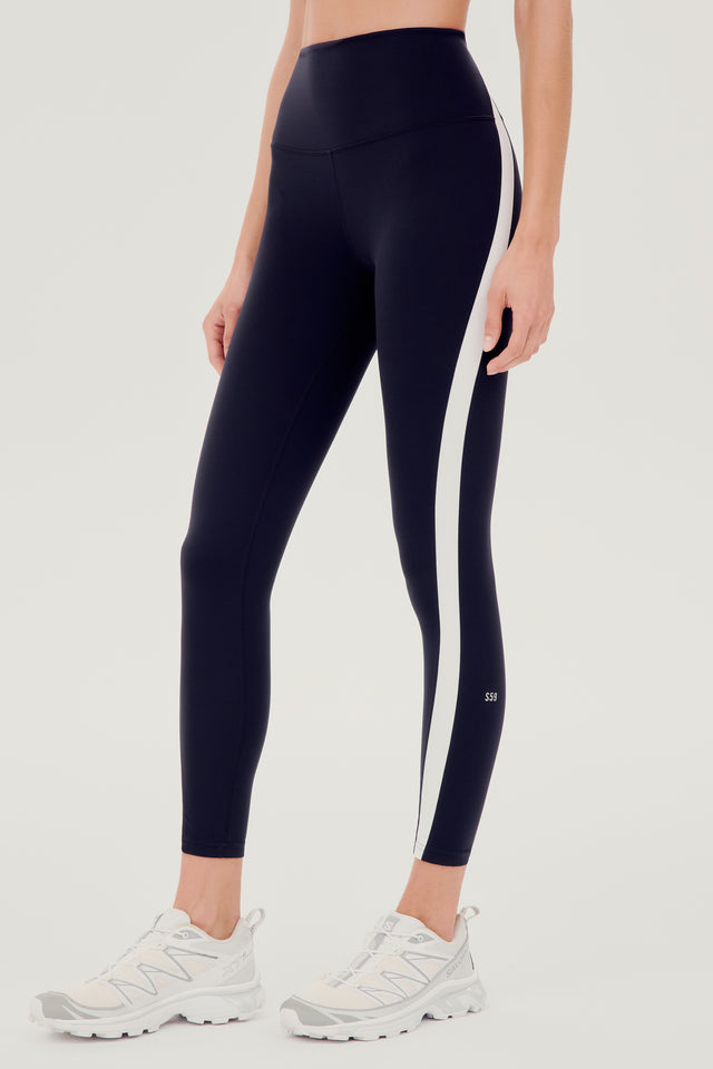A woman in SPLITS59 Miles High Waist Rigor 7/8 - Black/White sports leggings designed for yoga.