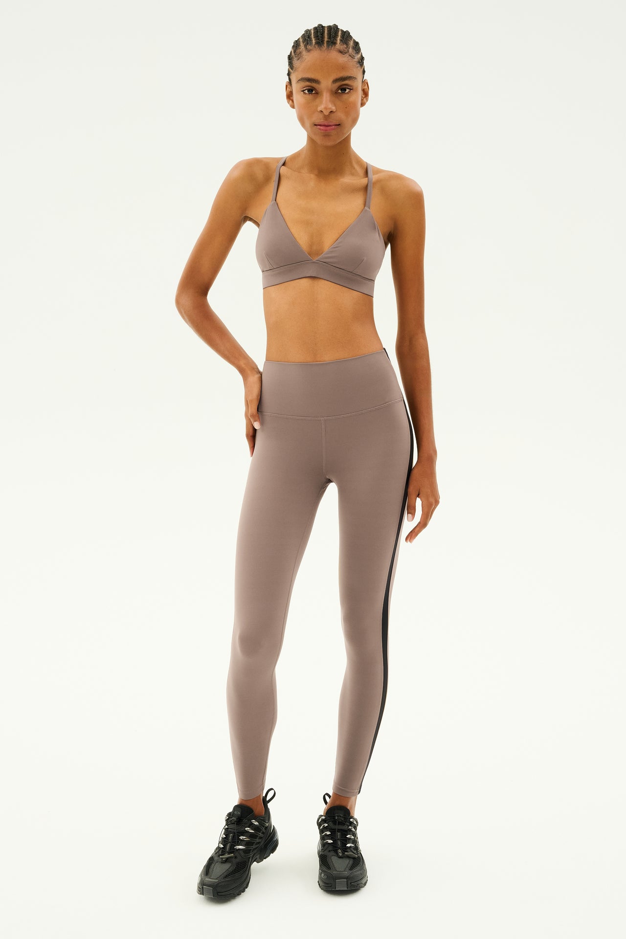 Standing against a plain white background, the person wears the Theo Rigor Bra in Lentil from SPLITS59, paired with leggings crafted from an ultra-luxe fabric. Complemented by sleek black shoes, this ensemble is perfect for multi-sport performance.