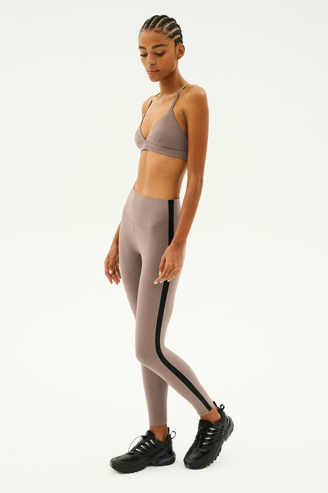 A person wearing a SPLITS59 Theo Rigor Bra in Lentil and tan leggings featuring black stripes, crafted from ultra luxe fabric, stands in black sneakers against a plain background.