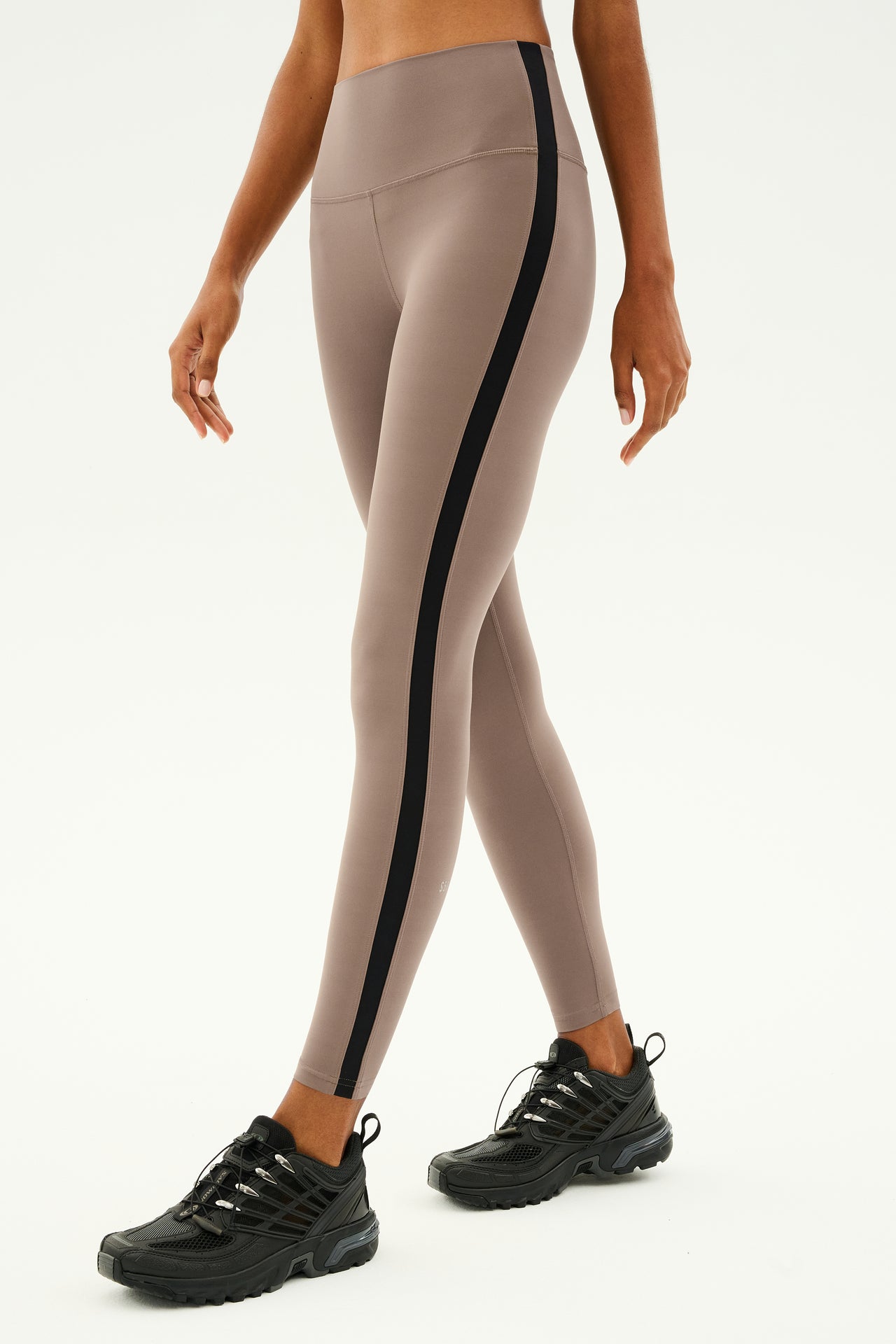 Close-up of a person wearing SPLITS59's Clare High Waist Rigor 7/8 leggings in Lentil/Black with black sneakers, showcasing the high-performance Rigor fabric against a plain background.