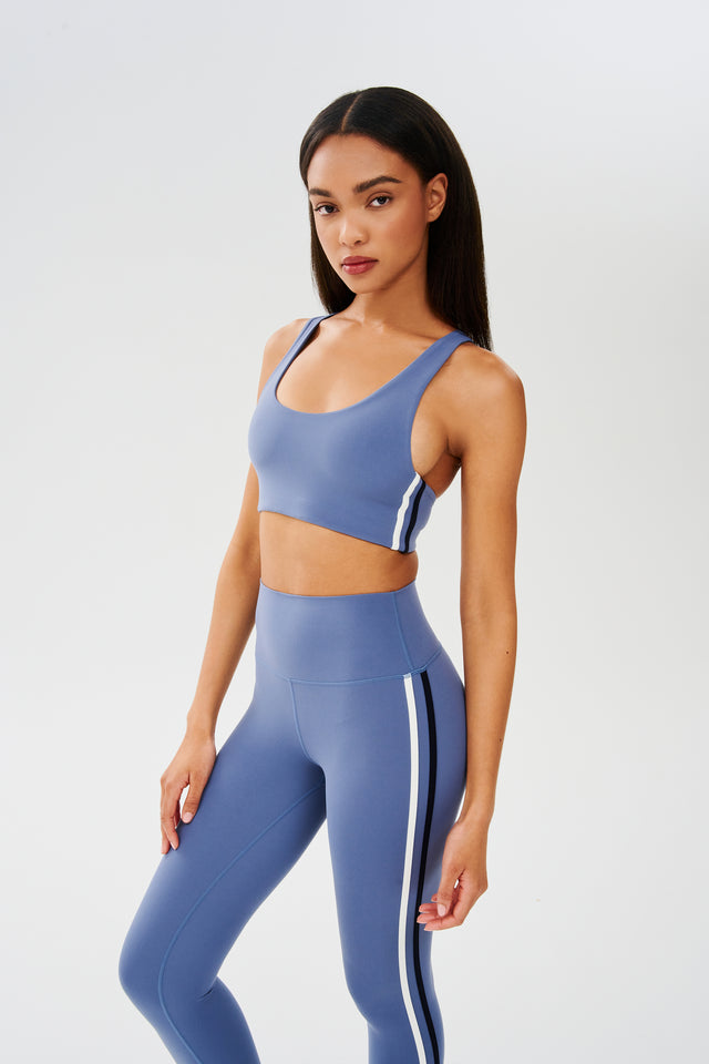 Side view of girl wearing light blue sports bra with thin black and white stripes down the side and light blue leggings 