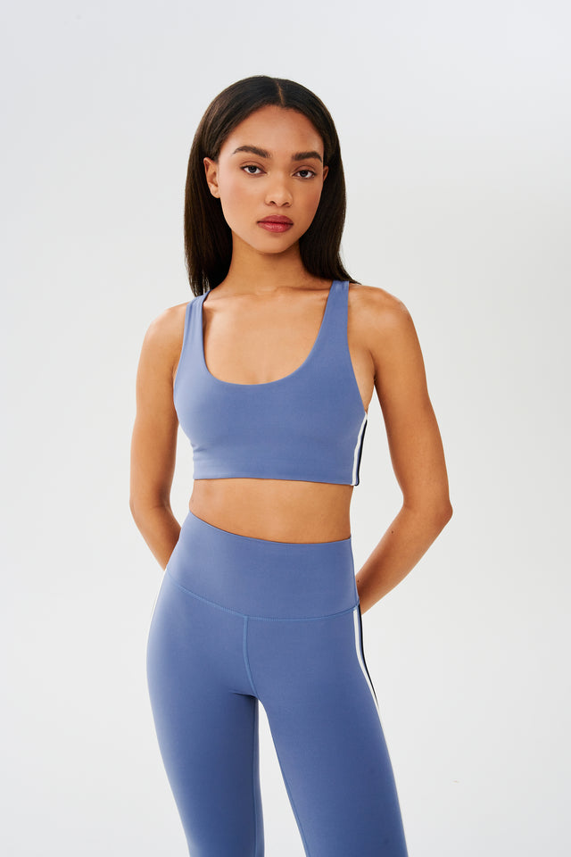 Front view of girl wearing light blue sports bra with thin black and white stripes down the side and light blue leggings