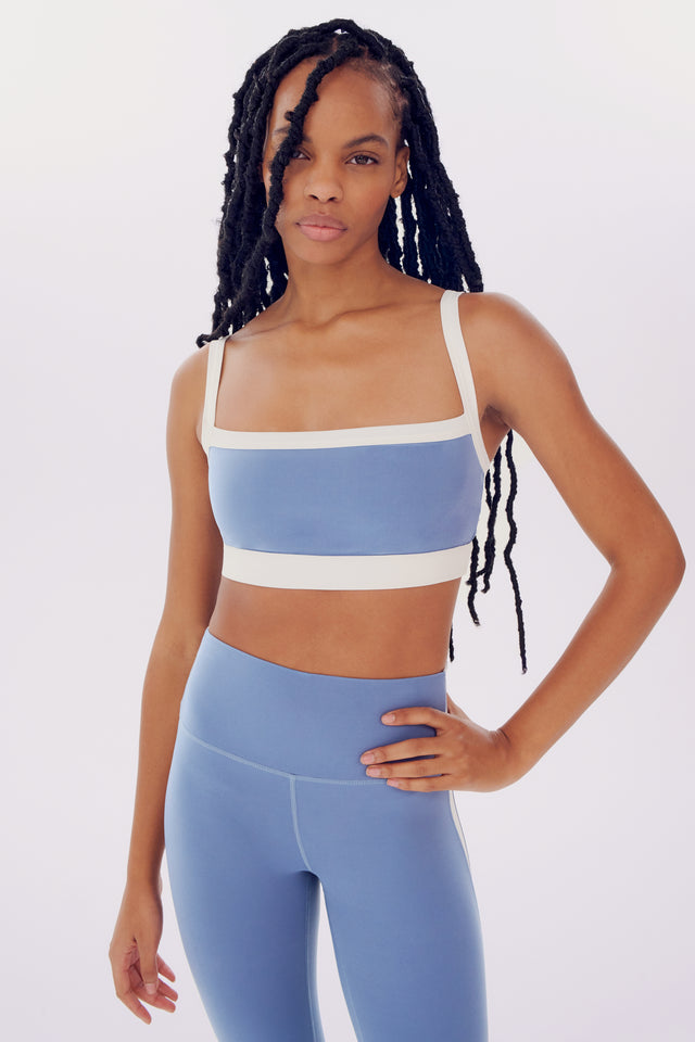 A young woman in a SPLITS59 Monah Rigor Bra - Steel Blue/White and leggings posing confidently against a plain white background.