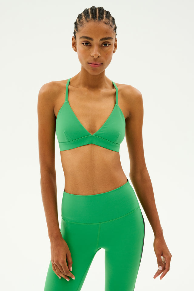 A person wearing a vivid grass-colored SPLITS59 Theo Rigor Bra and leggings, made from luxurious Rigor fabric, stands against a plain background, embodying the elegance of multi-sport performance.