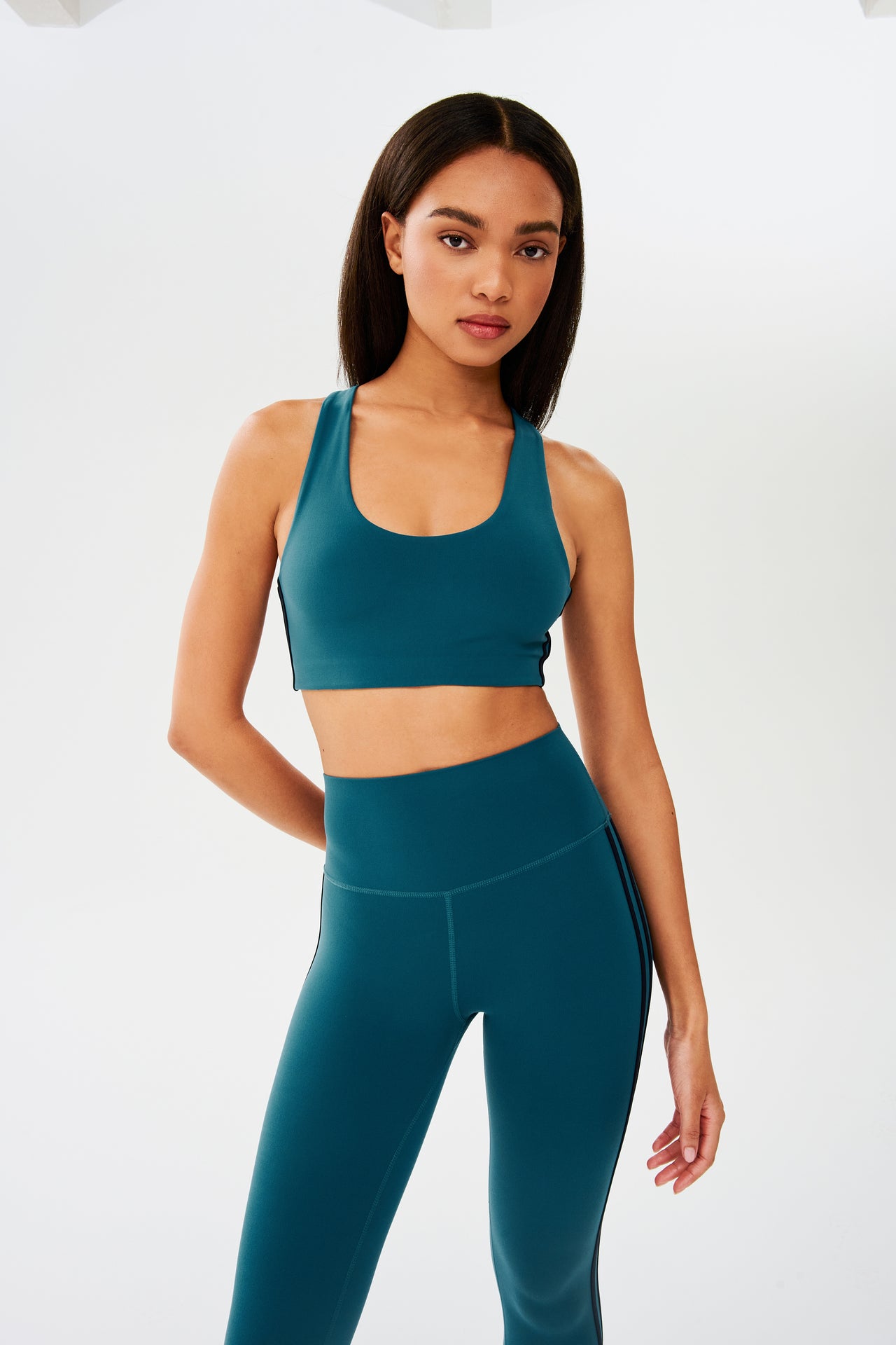 Front view of girl wearing greenish blue sports bra with two thin black stripes down the side and greenish blue leggings 