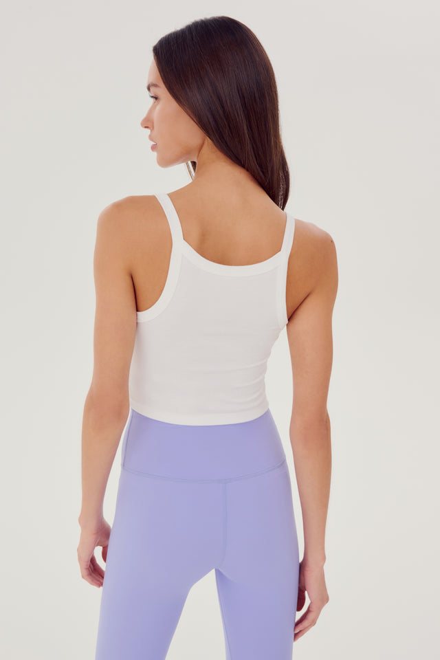 Back view of girl wearing white ribbed square neck cropped tank top with light purple leggings and white shoes