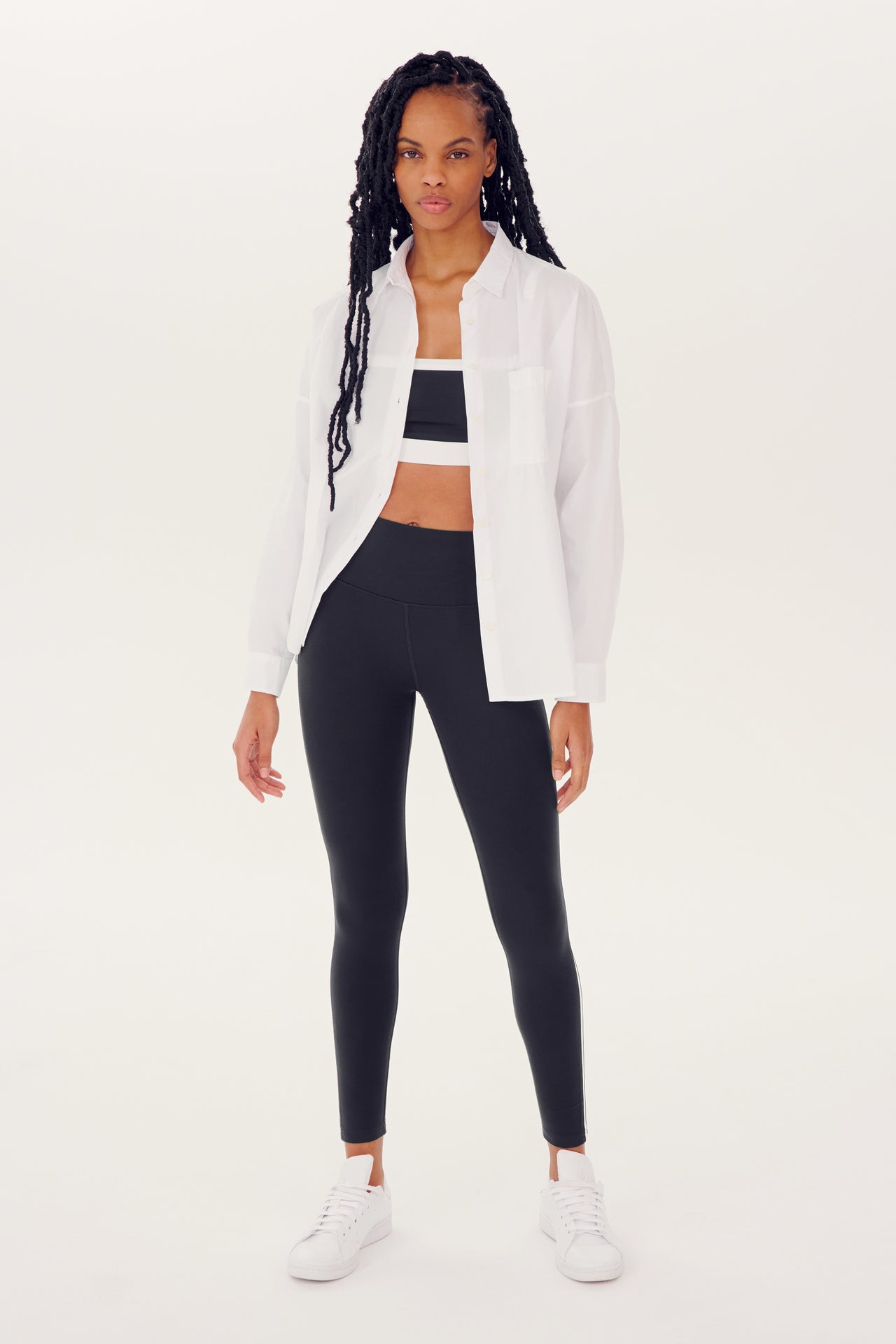Woman posing in an oversized Alex Mill x Splits59 Jo Shirt - White, black leggings, and white sneakers.