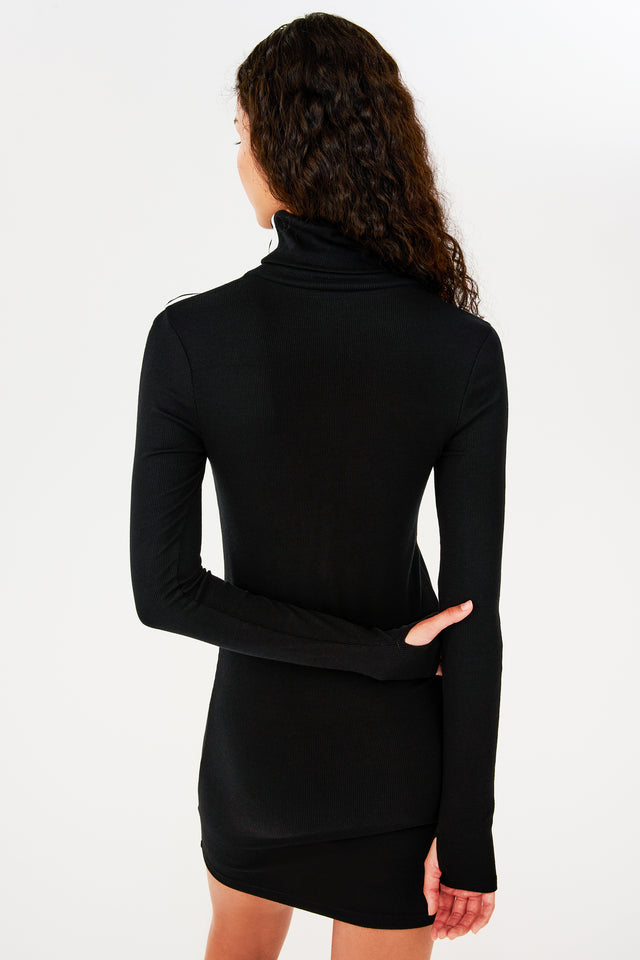 The back view of a woman wearing a black SPLITS59 Jackson Rib Turtleneck Dress.