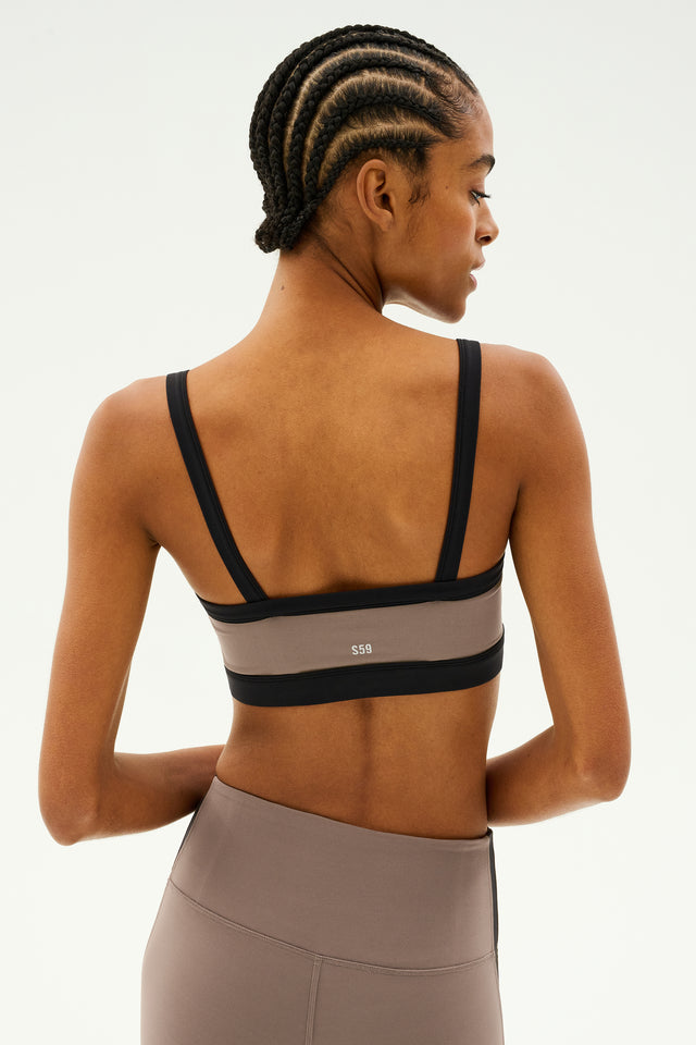 A person with braided hair is shown from the back against a plain background, wearing the SPLITS59 Monah Rigor Bra in Lentil/Black paired with leggings, ready for gym workouts.