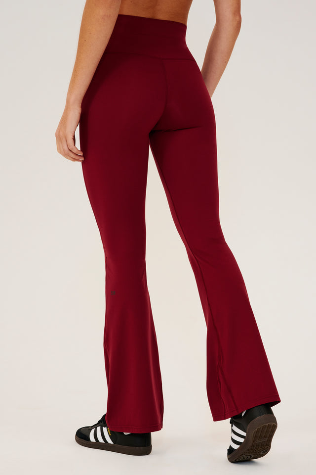 Back view of dark red high waist below  ankle length legging with wide flared bottoms with black S59 logo on back of left calf. Paired with black shoes with white stripes. 