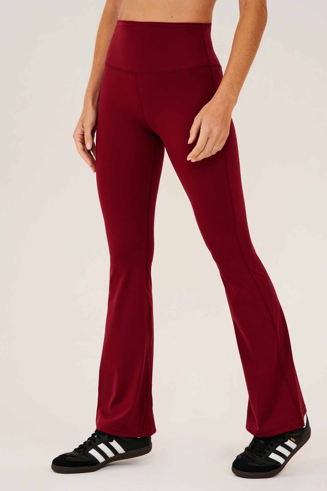 Frontview of dark red high waist below ankle length legging with wide flared bottoms. Paired with black shoes with white stripes.