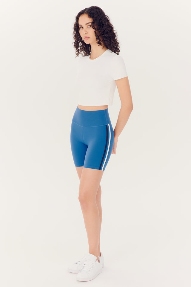 Woman standing in an SPLITS59 Airweight S/S Crop - White and blue nylon shorts against a white background.