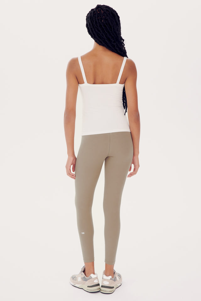 A woman in a SPLITS59 Romy Rib Tank - White and olive green leggings, seen from the back, standing against a white background.