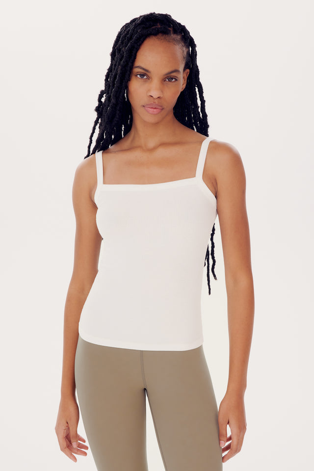 A woman with long braided hair wearing a SPLITS59 Romy Rib Tank - White and olive pants, standing against a white background.
