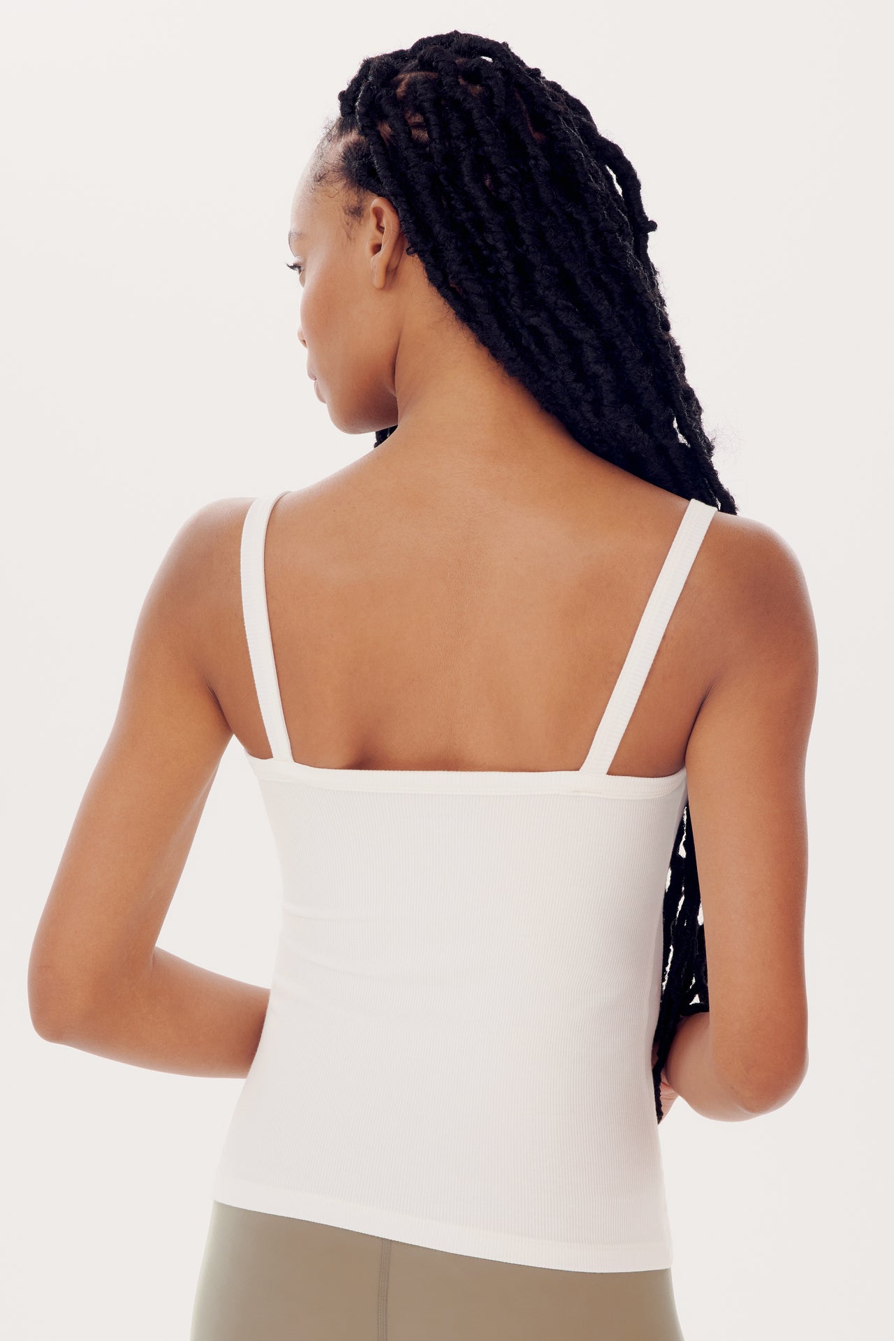 A woman seen from behind, wearing a SPLITS59 Romy Rib Tank - White and khaki pants, her dark braided hair draped over one shoulder.
