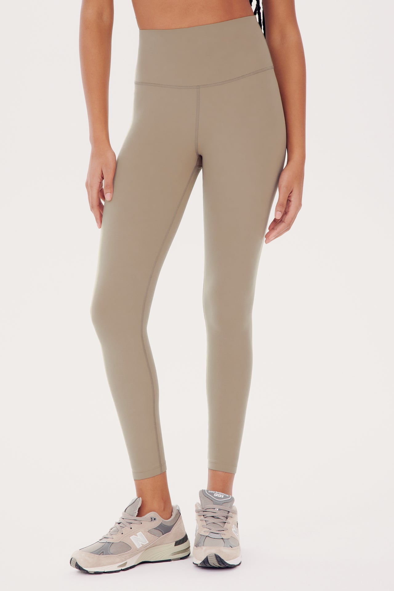 Woman wearing SPLITS59 Sprint High Waist Rigor 7/8 - Latte leggings and gray sneakers standing against a white background.
