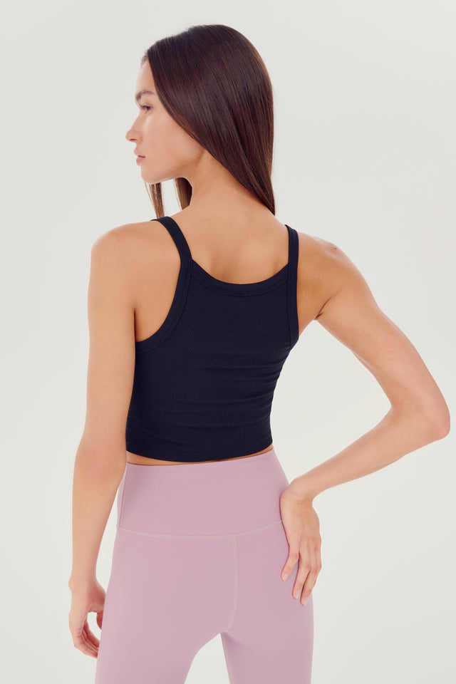 Back view view of girl wearing black ribbed square neck cropped tank top with light pink leggings