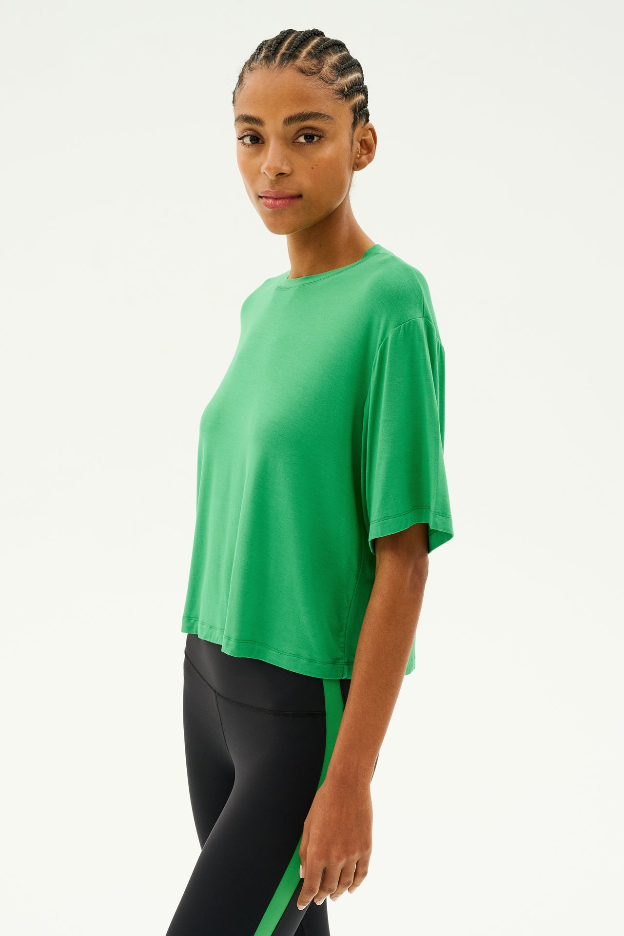 A person wearing the Djuna Oversized Jersey Tee in Grass by SPLITS59 and black leggings with a green stripe stands against a plain background, ready for running or gym workouts.