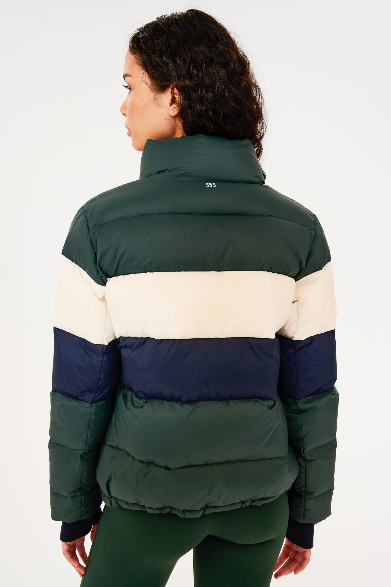 Back view of girl wearing dark green puffer jacket with blue and white stripes on arms and sleeve cuffs with thumb holes