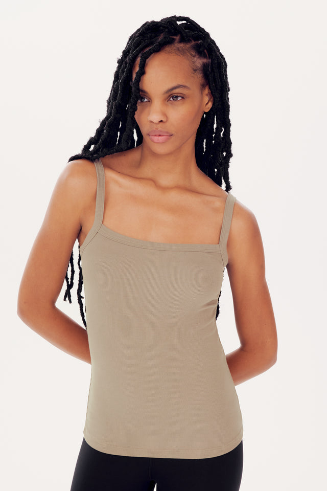 A woman with long braided hair wearing a SPLITS59 Romy Rib Tank in Latte, featuring a square neckline, standing confidently against a white background.