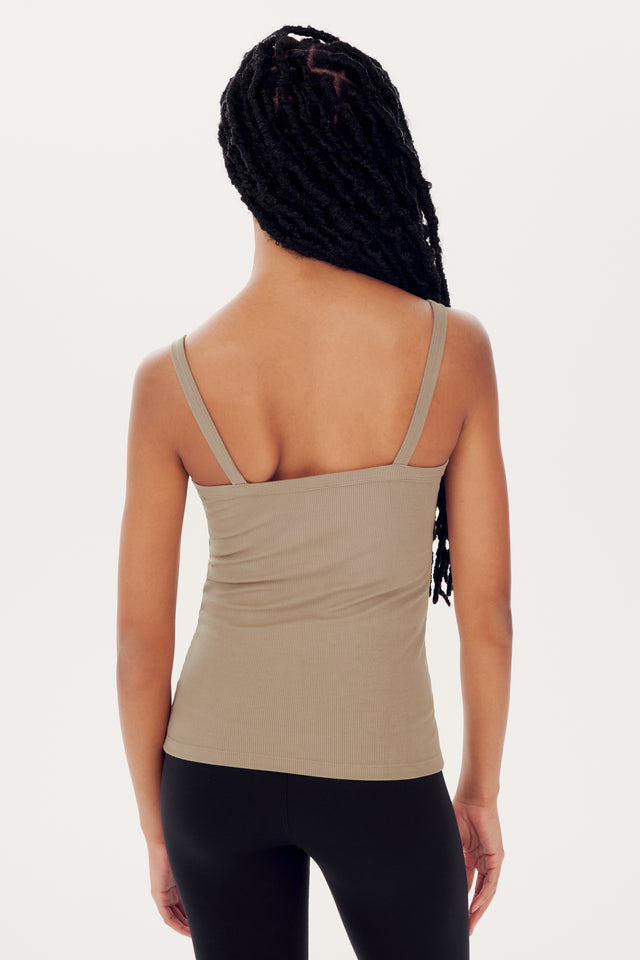 A woman with long braided hair wearing a SPLITS59 Romy Rib Tank in Latte with a square neckline and black leggings, viewed from behind against a white background.