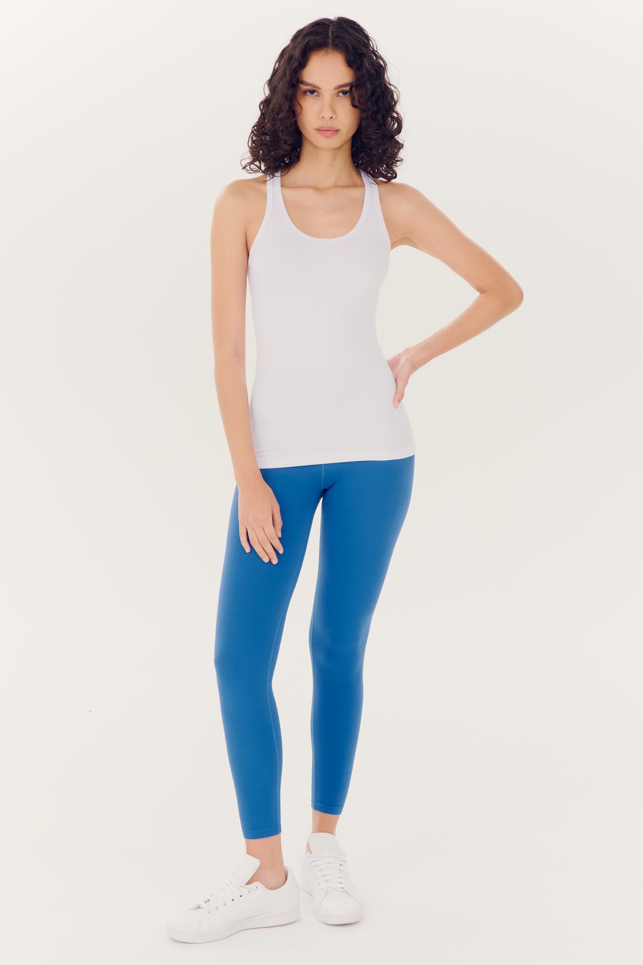 A woman posing in a white tank top and SPLITS59 Airweight High Waist Legging - Stone Blue against a white background.