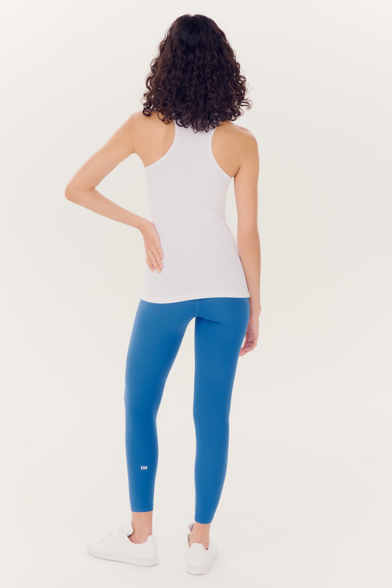 Woman wearing white tank top and SPLITS59 Airweight High Waist Legging - Stone Blue leggings standing with her back to the camera.