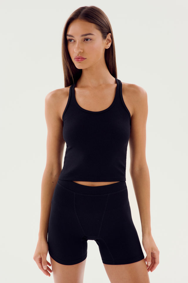 A person with long hair wearing an Ashby Rib Crop - Black by SPLITS59 and black shorts, perfect for gym workouts, stands against a plain white background.