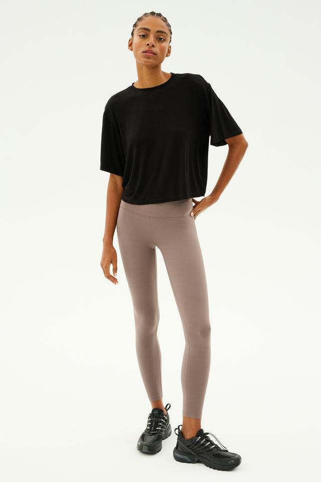 A person in a black shirt, Sprint High Waist Rigor 7/8 in Lentil by SPLITS59, and black shoes stands against a plain background.