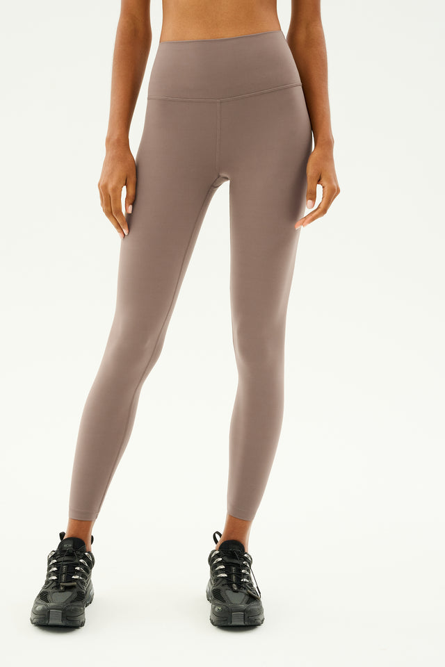 A person wearing SPLITS59 Sprint High Waist Rigor 7/8 leggings in Lentil and black sneakers stands against a plain background, ready for workouts.