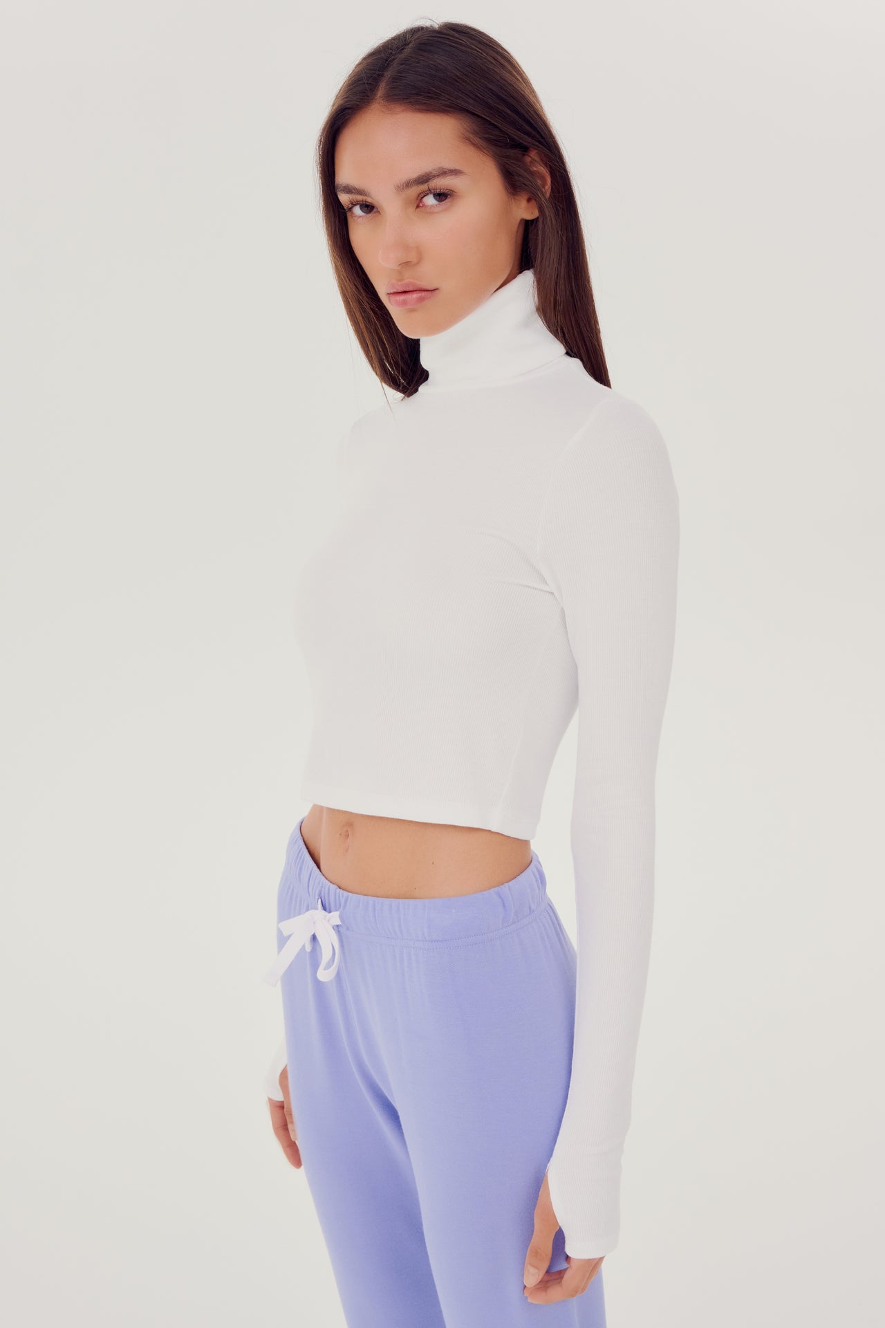The model is wearing a white SPLITS59 Jackson Rib Cropped Turtleneck top and purple high waist leggings.