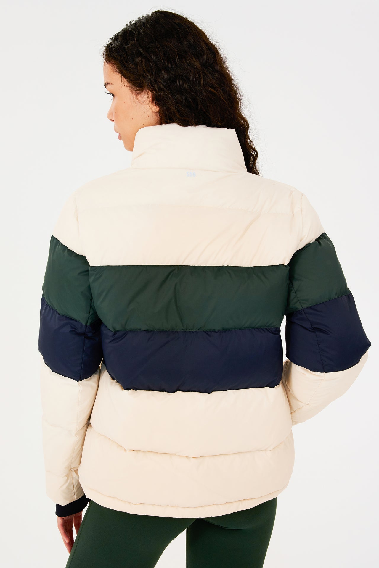 Back view of girl wearing white puffer jacket with blue and green stripes on arms and sleeve cuffs with thumb holes 