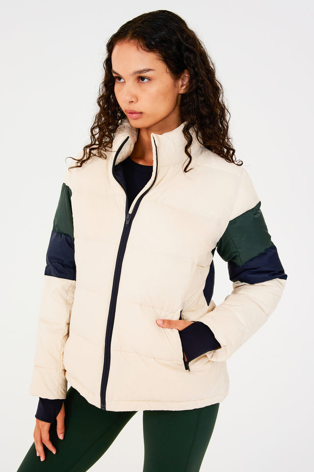 Front view of girl wearing white puffer jacket with blue and green stripes on arms and sleeve cuffs with thumb holes 