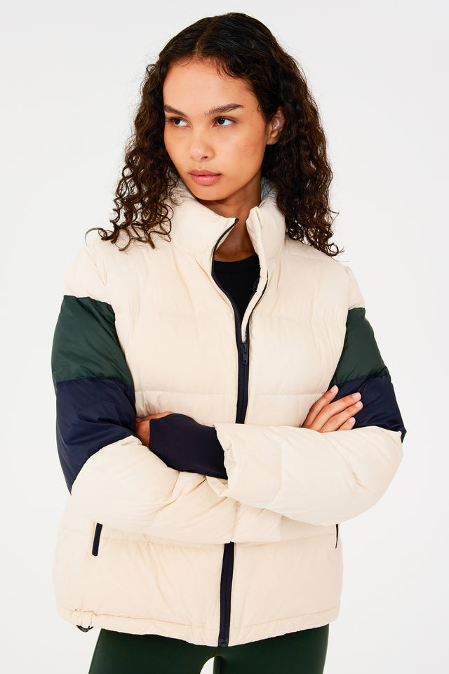 Side view of girl wearing white puffer jacket with blue and green stripes on arms and sleeve cuffs with thumb holes 