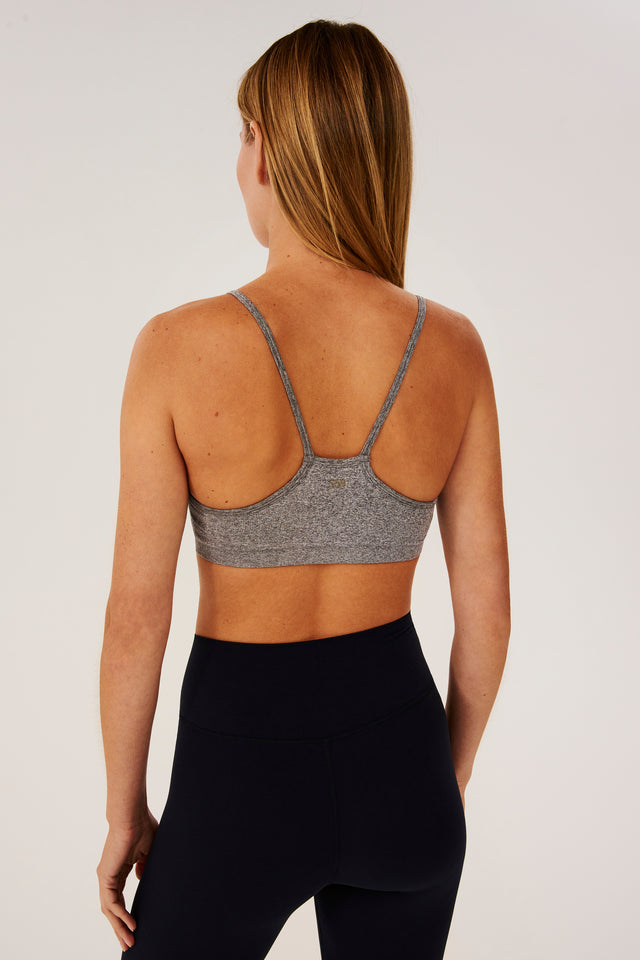 The back view of a woman wearing black leggings and a Splits59 Loren Seamless Bra in Heather Grey.