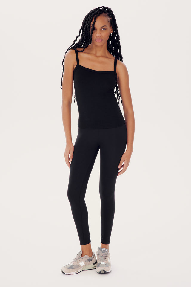 Young woman in SPLITS59's Romy Rib Tank - Black and leggings standing in a neutral pose against a white background.
