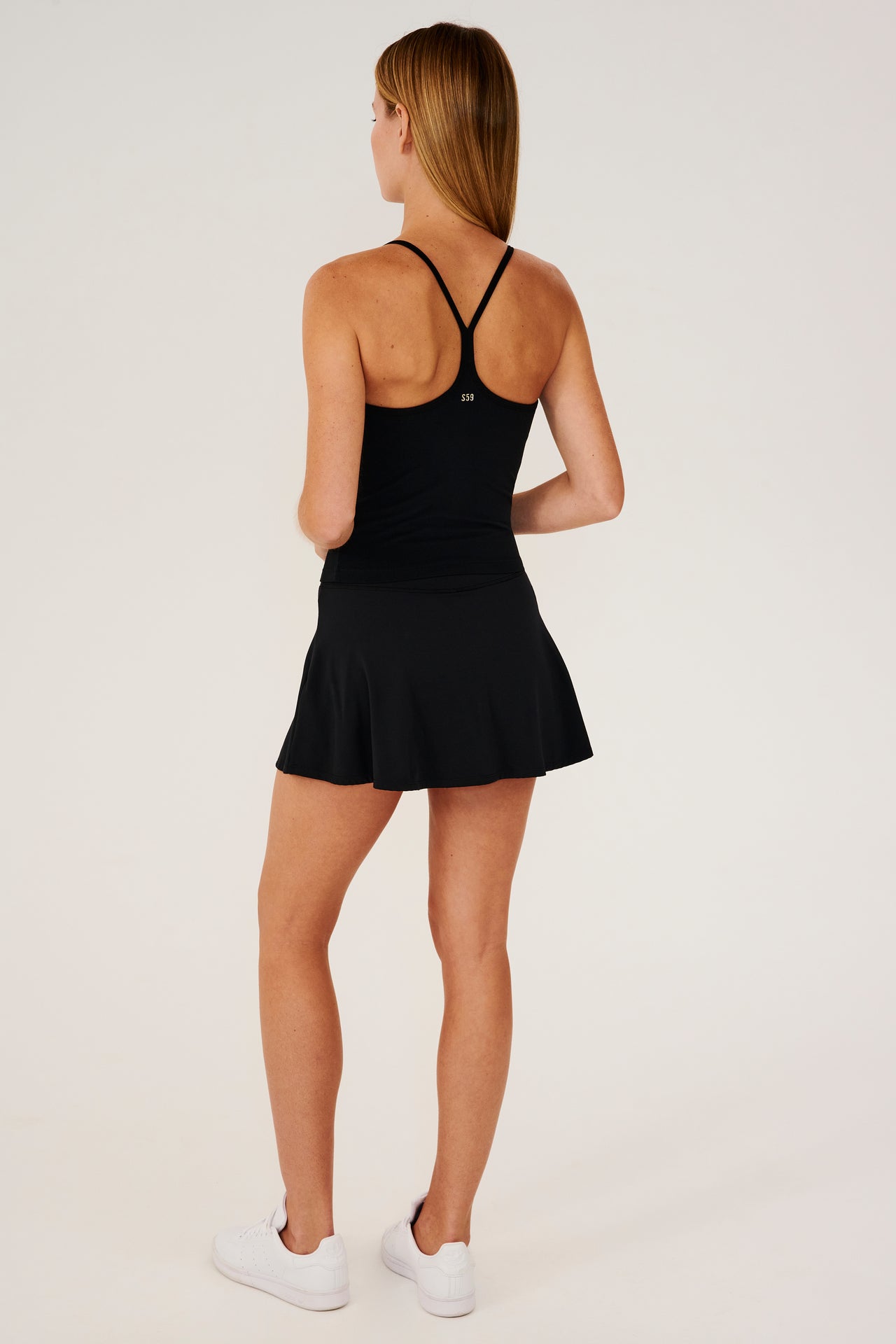 Full back view of girl wearing black upper thigh skirt with built in shorts, black tank top and white shoes