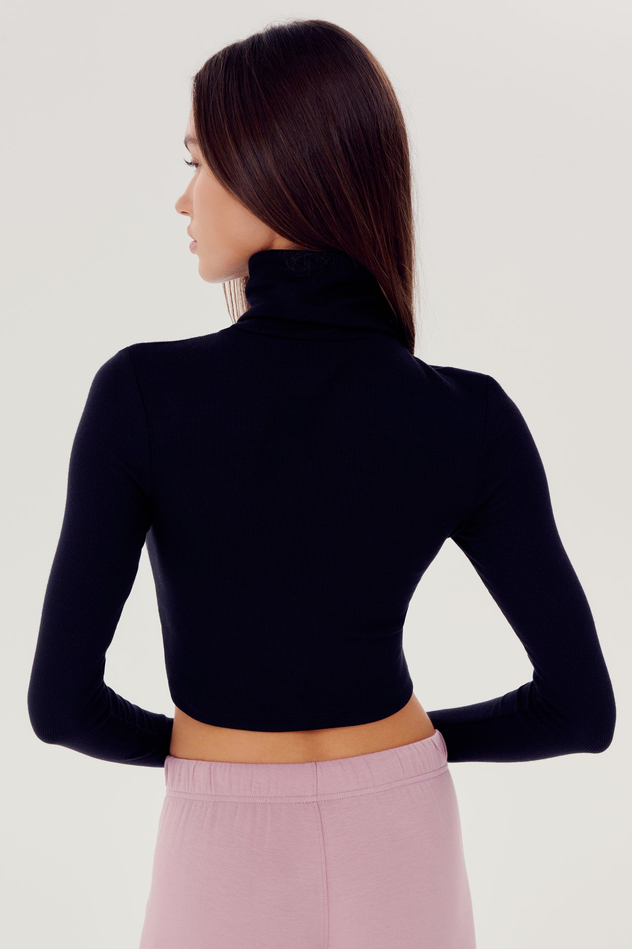The back view of a woman wearing a cropped length SPLITS59 Jackson Rib Cropped Turtleneck top and high waist leggings.